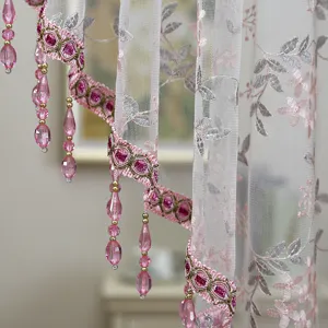 Close-up detail of white mesh curtain featuring pink floral embroidery and hanging crystal bead fringe.