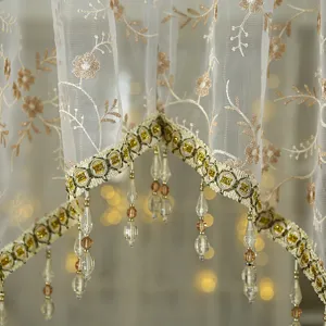 Close-up detail of vintage French lace short curtain with floral embroidery and beaded fringe.