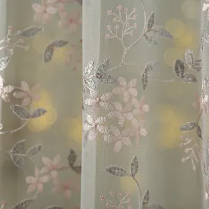 Close-up detail of sheer door curtain with delicate pink floral embroidery and soft light bokeh.