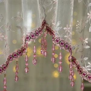 French vintage lace curtain detail, delicate floral embroidery with pink beaded tassels.
