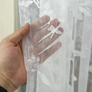 Close-up view of white sheer lace curtain detail, showing soft fabric texture and floral pattern.