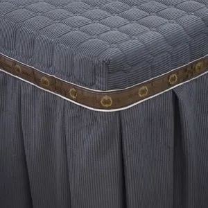 Nahaufnahme des grauen Cord-Steppbezugs mit dekorativer brauner Blumenband-Borte fur Details.