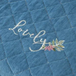Close-up detail of blue quilted cotton linen fabric with elegant white embroidery lettering.