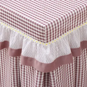 Checkered table cover detail with white lace and yellow daisy embroidery, soft fabric texture.