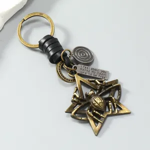 Detailed macro view of a vintage bronze-toned metal spider and star keychain with leather cord