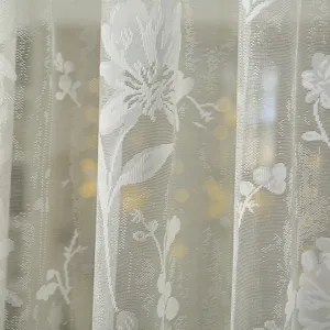 Close-up detail of white lace curtain fabric featuring delicate floral embroidery patterns.