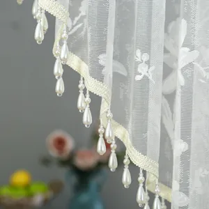 Close-up of white lace curtain detail featuring elegant pearl drop fringes and floral embroidery.