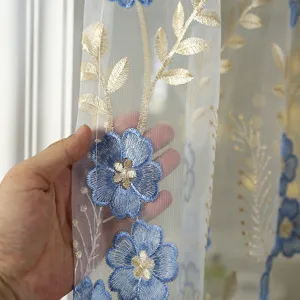 Close-up detail of sheer curtain with blue floral and gold leaf embroidery fabric texture.
