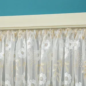 Close-up detail of white lace half curtain with embroidered floral and gold vine pattern.