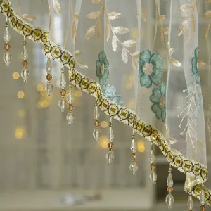 Detailed shot of sheer lace curtain with floral embroidery and beaded fringe trim for home decor.