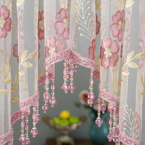 Close-up of pink floral lace sheer curtain with beaded fringe, elegant home decor detail.