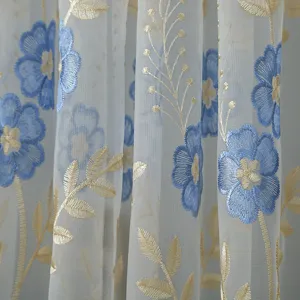Close-up detail of sheer curtain fabric featuring delicate blue floral embroidery.