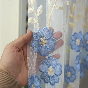 Detailed close-up view of sheer lace curtain fabric showcasing blue embroidered floral design.