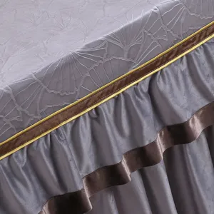 Nahaufnahme des grauen Stofftischbezugs mit edler Goldrandverzierung und feinen Rüschen.