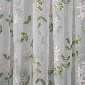Close-up detail of sheer curtain fabric with delicate green leaf and pink flower embroidery.