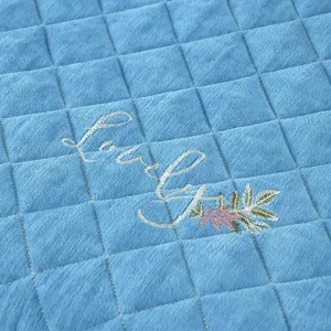 Close-up detail of blue quilted electric heating table cover fabric with elegant embroidery.