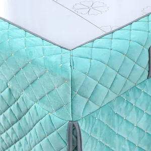 Close-up detail of teal quilted heating table cover with gold dots and gray piping edges.