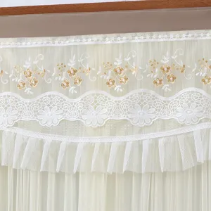 Close-up detail of sheer lace door curtain with delicate gold floral embroidery and ruffles.