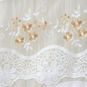 Detailed view of white mesh curtain fabric with gold floral embroidery and lace trim.