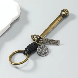 Gedetailleerd aanzicht van vintage metalen microfoon-sleutelhanger met leren riem en tag.
