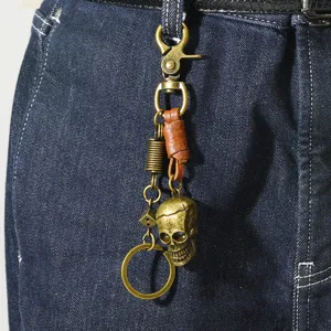 Porte-clés tête de mort vintage en bronze avec lanière en cuir sur un jean.