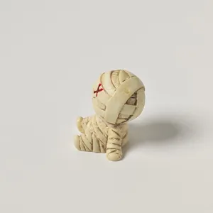 Close-up detail shot of a cute mini mummy figurine with wrapped bandages and red mark.