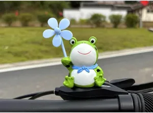 Close-up detail of a cute green frog figurine with blue flower accessory mounted on handlebar.