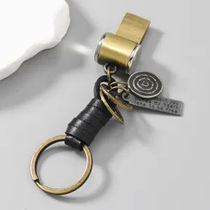 Detailed view of vintage metal whistle keychain with leather wrap and engraved charms.