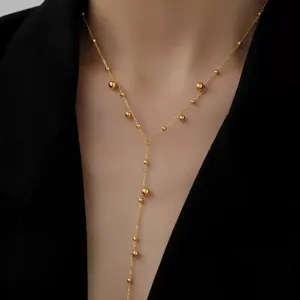 Detailansicht einer goldenen Y-Halskette mit Perlen vor einem schwarzen Hintergrund