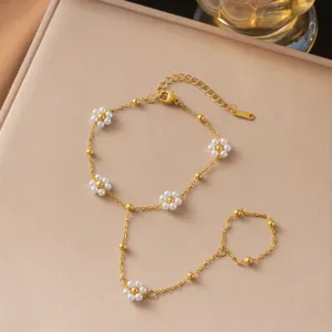 Detail eines goldenen Handketten-Armbands aus Edelstahl mit Perlenblumen-Charms.