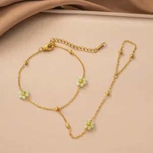 Detailansicht einer goldenen Handkette aus Edelstahl mit zarten grünen Blumenanhängern.