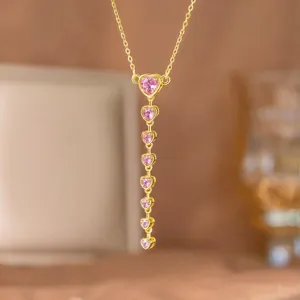 Close-up of elegant gold necklace featuring a vertical drop of pink heart-shaped zircons.