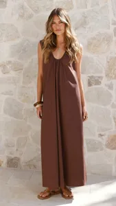 Detailed view of the elegant brown sleeveless U-neck maxi dress styled with a stone wall backdrop.