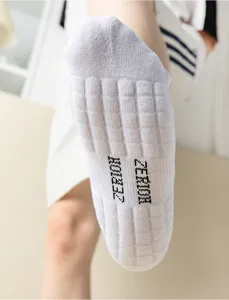 Detail shot of white athletic towel bottom socks featuring textured massage soles and knit brand logo.