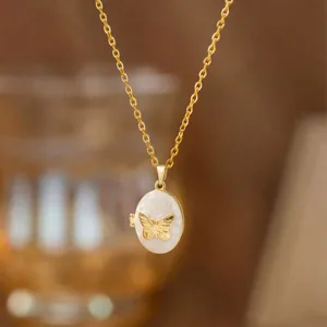 Vista detallada de un relicario de mariposa dorado estilo vintage con esmalte blanco