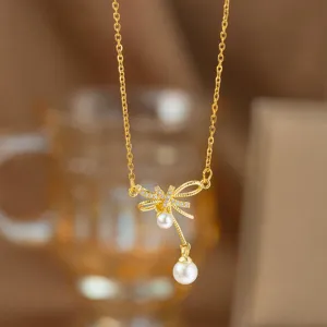 Detaillierte Nahaufnahme einer Halskette mit goldenem Schleifenanhänger und weißen Perlen