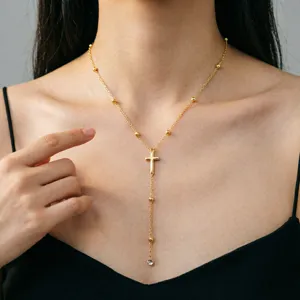 Nahaufnahme einer goldenen Y-Halskette mit Kreuz und Perlen an einem weiblichen Model