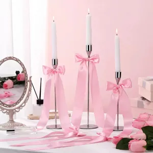 Detail shot of tall silver candlesticks decorated with elegant pink satin bows and white candles.