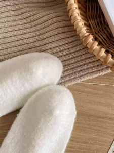 Close-up detail of soft white fluffy plush socks, cozy winter texture and warm home style.