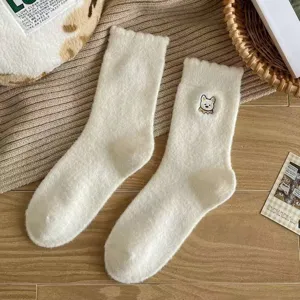 Close-up detail of cozy white fluffy winter socks featuring cute dog embroidery on wooden background.