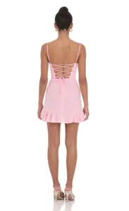 Detail view of the pink mini dress featuring a sexy lace-up back and playful ruffled hem.