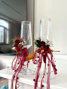Primo piano di flûte da champagne nuziali in fiori stabilizzati DIY con nastri rossi e perle.
