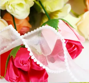 Dettaglio in primo piano di nastro in organza bianca con bordo perlato su rose colorate.