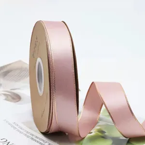 Gros plan sur le rouleau de ruban de satin rose avec des bords dores pour la decoration.