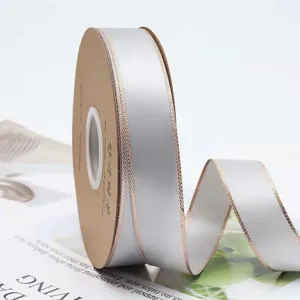 Gros plan detaille d'un rouleau de ruban satin gris clair avec bords dores doubles artisanat.