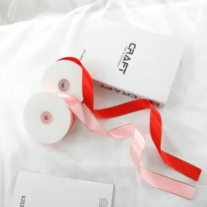 Detailed view of 2.5cm double gold-edged satin ribbon rolls in pink and red for gift wrapping.
