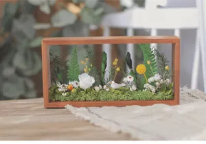 Vue détaillée d'un cadre photo en bois creux avec fleurs préservées et décors de mousse.