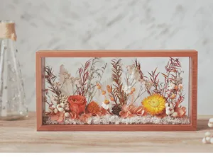 Détail du cadre d'ombre en bois avec arrangement de fleurs séchées aux tons chauds.