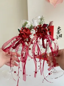 Vista dettagliata della decorazione per calici da champagne con fiori secchi rossi e nastri.