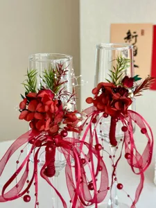 Bicchieri da champagne da matrimonio decorati con fiori stabilizzati rossi, nastri e perle.